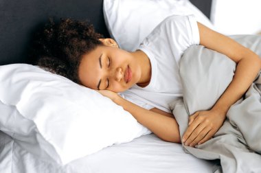 Sabah yatakta, tatlı rüyalar. Sakin Afro-Amerikan sevimli kıvırcık kız, yatakta tatlı tatlı uyuyor, rüyalar görüyor, dinleniyor, uyanmak ve yataktan çıkmak istemiyor. Uyku ve dinlenme konsepti