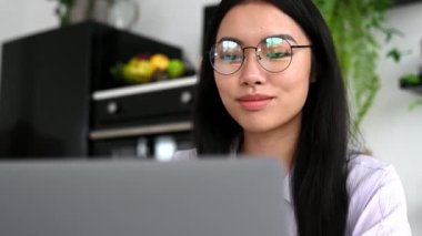Güzel, pozitif, zeki Asyalı esmer kız gözlüklü, tasarımcı, serbest çalışan ya da öğrenci, evde dizüstü bilgisayarın önünde oturuyor, çalışıyor ya da çalışıyor, başka tarafa bakıyor, projeyi düşünüyor, gülümsüyor.