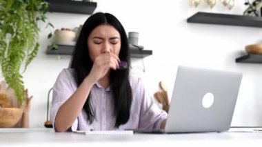 Yorgun Asyalı esmer kız, dizüstü bilgisayar başında çalışmaktan sıkılmış, stres, baş ağrısı, migren, gözlüğünü çıkarmış, burun köprüsüne masaj yapmış, dinlenmesi, uyuması gerekiyor.