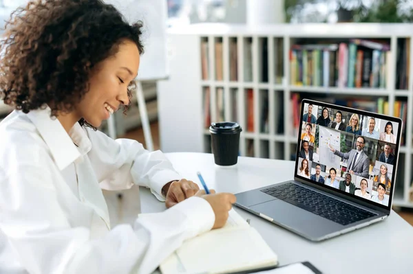 온라인 교육. 똑똑 한 아프리카계 미국 여자, 학생, 관리자, 경제학자, 컨설턴트는 노트북 앞에 앉아서 현대 사무실에서 온라인 교육을 받고 주의 깊게 듣고 필기를 합니다. — 스톡 사진