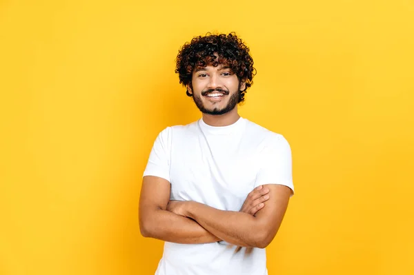 기본적 인 흰색 티셔츠를 입고 행복 한 긍정적 인 이란인 이자 아리아 출신의 곱슬머리의 남자, 광고, 발표, 고립된 오렌지 배경 위에 서서 웃으면서 — 스톡 사진