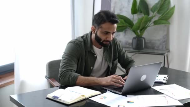 Happy excited lucky Indian or arabian man, business person, sits at a desk in modern office, got a good news, gesturing with his fists rejoicing in victory, success, good deal, big profit, smiling — Stock Video