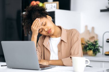 Çok çalışan Afrikalı Amerikan milenyum güzeli kız, öğrenci, serbest çalışan, uzaktan çalışmaktan bıkmış gözlerini kapamış, iş sırasında uykuya dalmış, uykuya, dinlenmeye, kahveye ihtiyacı var.