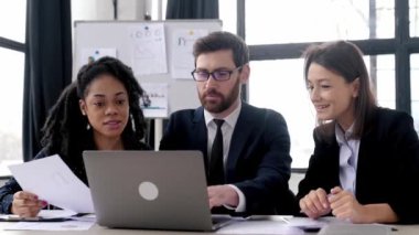 Bir projede iş ortakları birlikte çalışıyor. Çok ırklı meslektaşlar birlikte strateji üzerine beyin fırtınası yapıyorlar, modern ofiste oturup, belgeler üzerinde çalışıyorlar, dizüstü bilgisayar kullanıyorlar, tartışıyorlar, gülümsüyorlar.