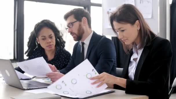 Intelligente, hübsche junge, erwachsene, brünette Geschäftsfrau im Anzug, sitzt am Arbeitsplatz in einem modernen Büro, während eines geschäftlichen Brainstormings mit Kollegen, schaut in die Kamera, lächelt freundlich — Stockvideo