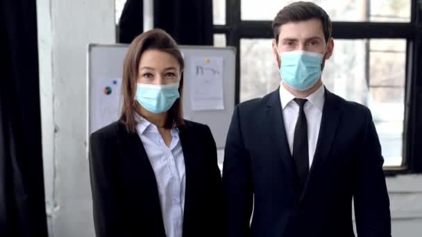 Élégants partenaires d'affaires caucasiens réussis, homme et femme positifs, debout dans le bureau, enlever leurs masques médicaux de protection de leur visage, sourire. Fin de la quarantaine et restrictions — Video