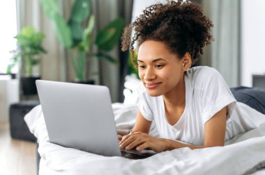 Şirin, Afro-Amerikan bir kız evde yatıp karnının üstünde yatar, dizüstü bilgisayar kullanır, internette gezinir, sosyal ağlarda sohbet eder, internetten web sitesi izler, e-posta yazar, gülümser.