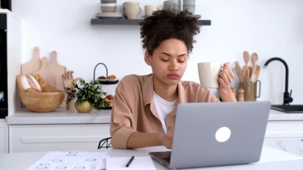 Gelangweilte Afroamerikanerin, Freiberuflerin, Designerin, die von zu Hause aus arbeitet, der langweiligen Online-Arbeit überdrüssig ist, unter chronischer Müdigkeit oder Überlastung leidet, eine Tasse Kaffee in der Hand hält, gähnt — Stockvideo