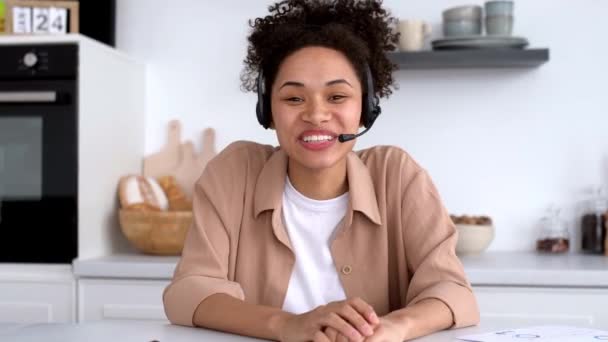 Mooie Afro-Amerikaanse stijlvolle meisje met headset, mentor of student, voert een online ontmoeting met collega 's of studenten, houdt een toespraak over bedrijfsideeën en plannen, glimlachen. Online lesconcept — Stockvideo