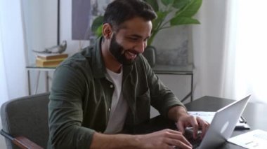 Mutlu, başarılı Hintli ya da Arap iş adamı, tüccar, broker, şirket CEO 'su, modern bir ofiste çalışıyor, istatistiklere odaklanıyor, finansal tablolara bakıyor, dizüstü bilgisayar kullanıyor, notlar alıyor, gülümsüyor.
