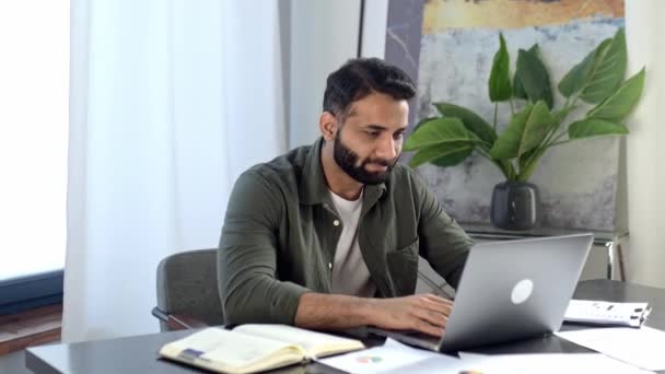 Retrato de un hombre carismático indio o árabe, vestido con estilo, empresario, freelancer o diseñador, sentado en un escritorio en una oficina moderna, mirando a la cámara, sonriendo amigable — Vídeos de Stock