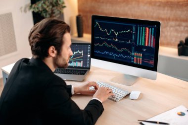 Yatırımlar, borsada ticaret. Başarılı beyaz erkek tüccar yatırımcı, kripto para piyasasını analiz ediyor, bilgisayara bakıyor, şifreli bir strateji geliştiriyor, riskleri analiz ediyor.