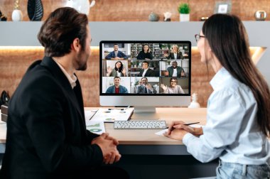 Brainstorm of business group. Business collaboration, caucasian man and woman, sit in a modern office in front of a computer screen, have an online video meeting with multiracial colleagues, smiling