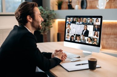 Çevrimiçi video konferansı. Kafkasyalı iş adamı, bilgisayarın önünde oturmuş, bir grup çok ırklı iş arkadaşıyla finansal brifing veriyor, finansal stratejileri tartışıyor, riskleri analiz ediyor.