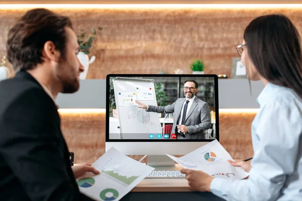 Online business briefing. Caucasian man and woman, sit in a modern office in front of a computer screen, have an online video meeting with mature successful ceo of company, analyze financial profit — Stock Photo, Image