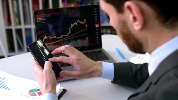 Exchange market. Smart man investor and crypto trader, using laptop and cellphone, analyzes charts of trading in stock market and digital cryptocurrency exchange,conducts analysis,trading crypto coins — Wideo stockowe