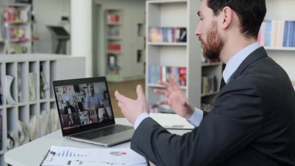 Homem de sucesso usando um laptop, realiza reunião virtual com parceiros de negócios em uma chamada de vídeo. Grupo de empresários multirraciais diversificados na tela do laptop realização de videoconferência — Vídeo de Stock