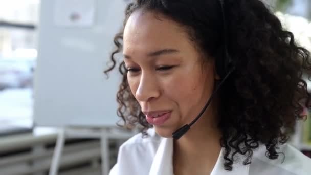 Close-up of successful pleasant curly woman, with headset, expert, consultant or call center operator, talks with client, smile friendly. Support service concept, hotline, distant communication — Stockvideo