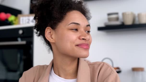 Positive lovely african american girl, freelancer, IT specialist, sit at home in the kitchen, looking away, dreaming, continues using laptop for work, texting with colleagues, working on project,smile — стокове відео