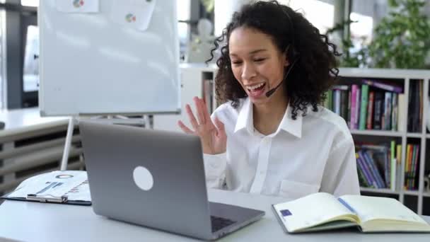 Framgångsrik smart afrikansk amerikansk kvinna, stödarbetare, online-konsult, call center arbetare, sitter vid sitt skrivbord framför en bärbar dator, har ett videomöte med en klient, gester, leende — Stockvideo