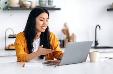 Uzaktan iletişim. Dost canlısı, güzel Asyalı esmer kız, menajer, serbest çalışan, mutfakta oturmuş, müşteriyle ya da çalışanlarla bilgisayar başında konuşuyor, projeyi tartışıyor, gülümsüyor.