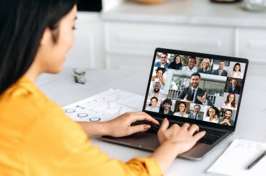Sanal toplantı, iş arkadaşlarının beyin fırtınası, online sohbet. Laptop ekranına bir kızın omuz üstü görüntüsü, çok ırklı iş grubuyla görüntülü konuşma, projeyi tartışma, yeni bir başlangıç.