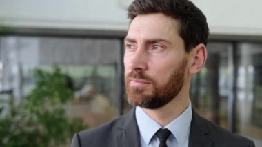 Başarılı, zeki, etkili, beyaz sakallı bir iş adamının yakın plan video portresi, üst düzey bir yönetici, ya da IT uzmanı, takım elbiseli, kameraya bakıyor, modern ofiste duruyor.