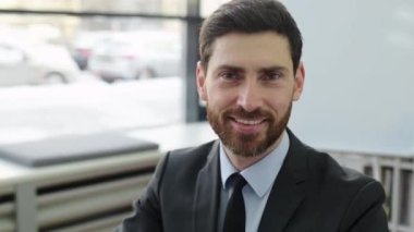 Olumlu, başarılı, zeki, zeki, beyaz sakallı bir iş adamı, avukat, üst düzey yönetici veya IT uzmanı portresi, kameraya bakıyor, modern bir ofiste oturuyor, dostça gülümsüyor.