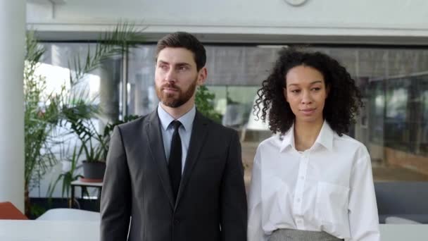 Two successful business people, caucasian man ceo of company, african american female top manager, in formal wear, are standing in modern office, looking at the camera, smiling, partnership concept — Stok video