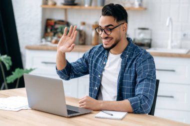 Pozitif Hintli ya da Arap adam, online öğretmen, serbest çalışan, öğrenci, gözlük takan ve günlük kıyafetler giyen, video konferansında konuşan, dizüstü bilgisayara bakan, sanal toplantı yöneten, evden çalışan, gülümseyen