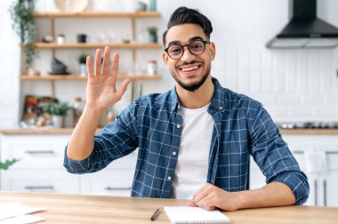 Çekici Hintli ya da Arap adam, evdeki masada oturuyor, webcam 'de konuşuyor, video görüşmesi yapıyor ya da müşteriyle ya da iş arkadaşıyla konuşuyor, danışman kayıt eğitimi alıyor, karşılama yapıyor, güler yüzlü arkadaş canlısı