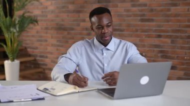 Focused african american businessman writing notes in notebook during online webinar, is improving qualifications. Smart black male student study online, listening online lecture, using laptop
