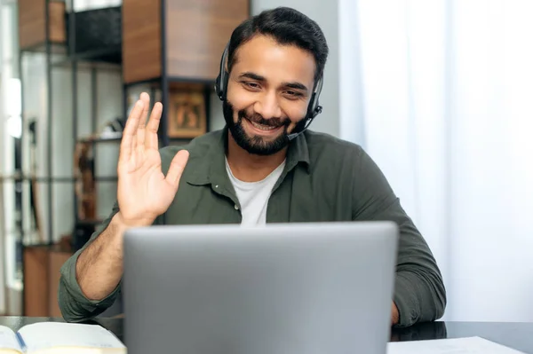 Online video consultation. Positive Arabian or Indian call center operator, hotline consultant, mentor, with headset, conducts online consultation with clients or online lecture with student, smiling