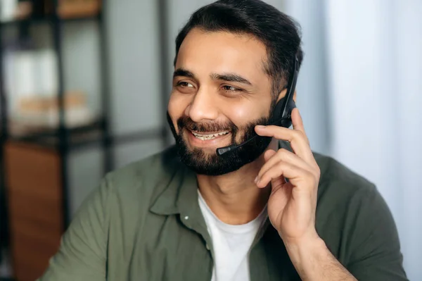 Support service concept. Close-up of friendly pleasant attractive Indian or Arabian man with headset, consultant or mentor, hotline expert, looks to the side, smiles friendly, conducts consultation