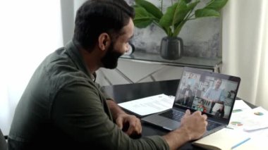 Sanal online toplantı, uzak görüşmeler. Başarılı bir yoğun ırk başarılı bir adam, modern ofiste çalışma masasında oturuyor, bilgisayar kullanarak video konferansı yoluyla çok ırklı iş ekibiyle konuşuyor.