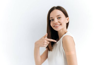 Beyaz tenli güzel mavi gözlü bir kız omzunda alçıyla izole edilmiş beyaz bir arka planda duruyor çeşitli hastalıklara karşı aşı oluyor, dokunulmazlık kazanıyor kameraya bakıyor, gülümsüyor.