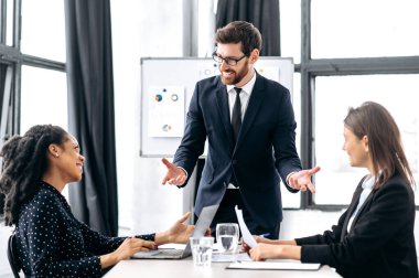 Çok ırklı çalışanların takım çalışması, işbirliği. Beyaz tenli çekici erkek patron, yeni bir iş projesiyle ilgili fikirleri tartışıyor, beyin fırtınası yapıyor, kadın ortaklarına finansal iş planlarını anlatıyor.