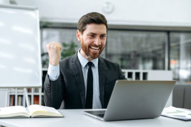 Modern ofiste bir dizüstü bilgisayar üzerinde çalışan mutlu beyaz iş adamı, şirket yöneticisi, programcı, finansör, şirketin gelişimi hakkında bir rapor alacak, projenin başarısına sevinecek
