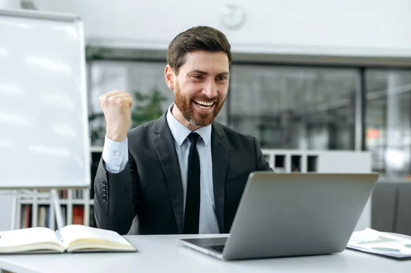 Happy caucasian joyful businessman, company manager, programmer, financier, working on a laptop in modern office, will receive a report on the development of the company, rejoice a success of project