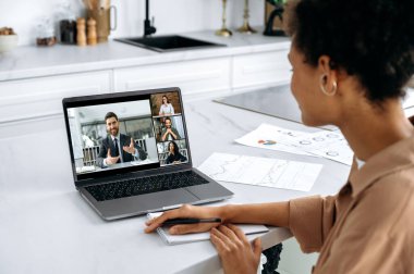 Çok ırklı insanlarla birlikte dizüstü bilgisayarlı Afrikalı Amerikalı kızın omuz üstü görüntüsü. İş arkadaşlarıyla beyin fırtınası yapan, laptop ve video konferansı kullanarak online web sitelerini dinleyen bir kadın.