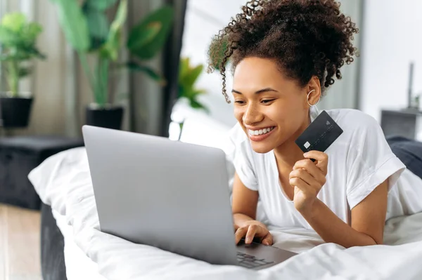 온라인 온라인 긍정적 아프리카 미국인 곱슬머리 집에서 침대에 노트북 카드를 — 스톡 사진