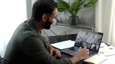 Sanal online toplantı, uzak görüşmeler. Başarılı bir yoğun ırk başarılı bir adam, modern ofiste çalışma masasında oturuyor, bilgisayar kullanarak video konferansı yoluyla çok ırklı iş ekibiyle konuşuyor.