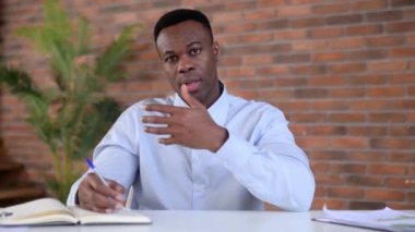 Web kamerası görüntüsüne yakın çekim, arkadaş canlısı, zeki genç siyah erkek, üst düzey yönetici, mali danışman, ofiste masada oturuyor, iş arkadaşlarıyla konuşuyor, video görüşmelerine katılıyor, notlar alıyor.
