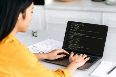 Ekranda programlama kodu olan bir dizüstü bilgisayarda çalışan Asyalı kadının omuz üstü görüntüsü. Yazılım ve kodlama teknolojisiyle çalışan akıllı profesyonel kadın programcı.