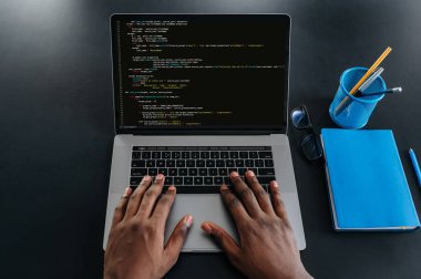 Erkek Afrikalı Amerikalıların dizüstü bilgisayarlı klavyesinin başında, bilişim uzmanı, programcı, modern bir ofiste oturmuş, bir web sitesi, uygulama, yazma kodları ve veri kodu geliştirme üzerinde çalışıyor.