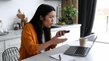 Teknoloji ve iletişim. Sinirli Asyalı kız, serbest çalışan, CEO, mutfakta oturmuş, stresli bir telefon görüşmesi yapıyor, gıcık çığlıkları bir akıllı telefona atıyor, duygusal bir sesli mesaj kaydediyor.