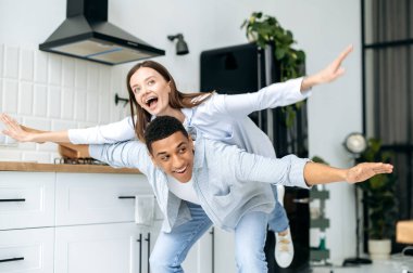 Genç mutlu çok ırklı çift evde eğleniyor. Neşeli bir çift, beyaz bir kız ve İspanyol bir adam evin içindeki mutfakta oynaşıyor, kız adamın arkasında, birlikte gülüyor.