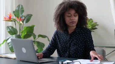 Odaklanmış Afrikalı Amerikalı kadın, serbest çalışan, yönetici, şirket CEO 'su, bir dizüstü bilgisayarın başında oturuyor, belgelerle yoğun çalışıyor, dinamikleri analiz ediyor, bir çalışma stratejisi geliştiriyor, iş planı hazırlıyor.