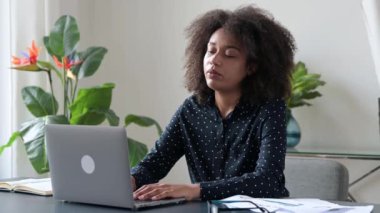 Yorgun, üzgün, Afro-Amerikan kıvırcık saçlı kız, menajer, ofis çalışanı, çalışma masasında oturuyor, dizüstü bilgisayarı kapatıyor, işi bitiriyor, yorgun hissediyor, aşırı çalışıyor, baş ağrısı, dinlenmeye ihtiyacı var.