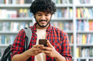 Kablosuz teknoloji konsepti. Mutlu Hintli ya da Arap milenyum adamı, serbest çalışan ya da öğrenci, akıllı telefonunu kullanıyor, sosyal ağlarda arkadaşlarıyla sohbet ediyor, mesajlaşıyor, internette geziniyor, arkadaşça gülümsüyor.